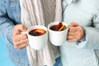 Couple in warm clothes with mugs of tasty mulled wine on blue background, closeup