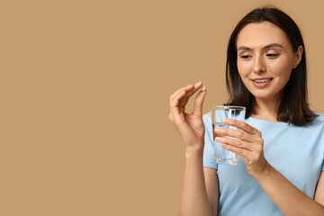 Sticker - Pretty young woman with pill and glass of water on brown background