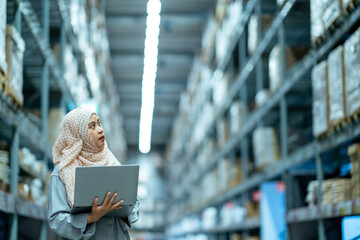 Wall Mural - Portrait of Asian muslim female headscarf hijab holding computer laptop checklist product shelves warehouse. woman worker inspecting goods industry. Logistic concept.