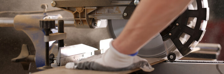 Man in protective gloves works with miter saw cutting board