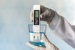 pH meter in hands with gloves, glass of water on blue background. Measurement of the characteristics of drinking water. The hardness of the water. poor water quality. high values of salt impurities