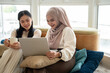 © bongkarn - An Asian-Muslim woman is watching videos or a movie on a laptop with her friend in a room together.