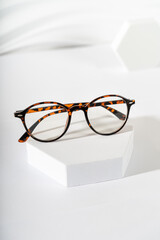 Poster - Unisex eyeglasses in a tortoiseshell plastic frame on podium on white background. Vertical, close up. The product minimal still life. Optic store discount, sale. Copy space. Trendy eyewear photography