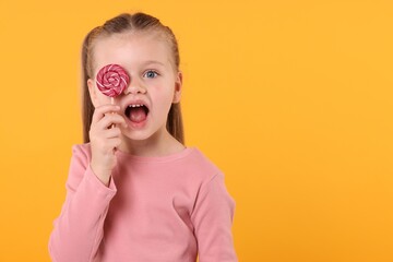 Wall Mural - Emotional little girl covering eye with bright lollipop swirl on orange background, space for text