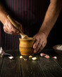 The chef crushes the garlic with a wooden pestle and mortar. We are preparing a national dish. Close-up of a chef's hands while working. Peasant products