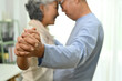 © Prathankarnpap - Romantic elderly couple spouses dancing in living room and looks at each other with love
