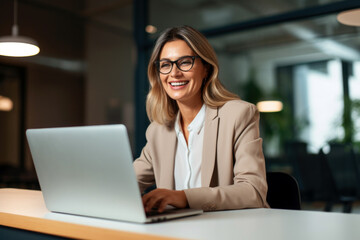 Wall Mural - Happy mid aged business woman working on laptop in office. hr manager communicating by conference call, remote online job interview on laptop