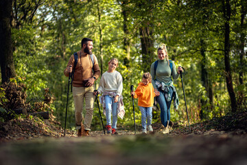 Wall Mural - Smiling family of four exploring nature on a scenic forest hike.