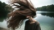 Dynamic capture of flowing brown hair moved by the wind, with a serene lake and lush forest as the backdrop. The subject exudes a sense of freedom and connection to nature.