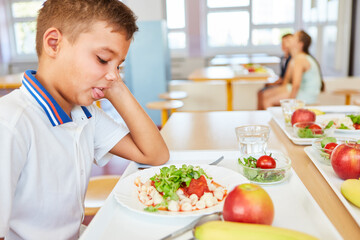 Wall Mural - Boy sticking out tongue sitting in school cafeteria