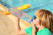 Cute little boy drinks water from a plastic bottle against the background of a swimming pool. Summer thirst, dehydration on vacation. The benefits of drinking water.