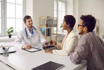 Happy black married couple visiting and consulting with family doctor. General practitioner gives therapy prescription to patients. Healthy young husband and wife get good health exam analysis results