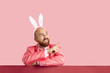 Funny man in suit and headband with Easter bunny ears shows on copy space on pink background. Caucasian young bald bearded man in pink formal suit points finger to side. Advertising banner.
