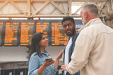 Fototapeta  - Group of multiracial friends checking time on departure board at a railway train station before boarding train. Enjoying travel by train concept