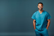 portrait of happy poc medical male staff wearing scrubs isolated on plain blue studio background, with copy space