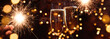 Toasting champagne for festive celebrations. Glasses of sparkling wine in front of golden bokeh lights and glowing sparklers. Horizontal background for christmas, new year, parties and festive events.
