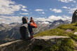 © Guzel - Gray-haired male traveler with backpack sitting on rock and taking pictures of mountain landscape, Austria