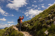 © Guzel - Man with backpack standing on trail with taking pictures of further route against the background of picturesque sky