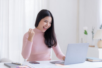 Happy young Asian woman raising hands with victory smiling happily with laptop at home. Success, win, victory, triumph, congratulation, concept.