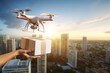Selective focus at hand receive a package from flying delivery drone on the rooftop and blur background of city skyline and sunny sky.