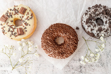 Wall Mural - Set of assorted colorful white and dark chocolate glazed donuts with mixed sprinkles on paper closeup on stone table. Top view sweet pastry card.