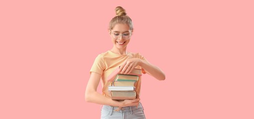 Wall Mural - Young woman with stack of books on pink background