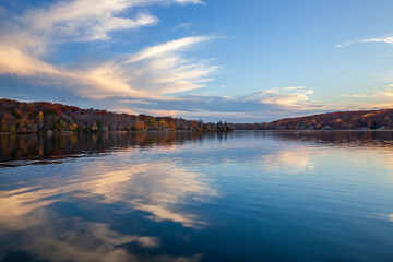 Wall Mural - calm lake in minnesota with hills and trees in autumn color below beautiful clouds at sunset