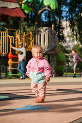 Wall Mural - Cute kid baby in a jacket stands on the playground