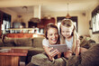 Happy young woman holding a smartphone with daughter on the couch at home