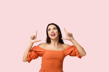 Wall Mural - Beautiful young happy woman pointing at something on pink background