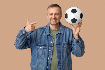 Canvas Print - Handsome mature man pointing at soccer ball on brown background