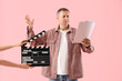 © Pixel-Shot - Mature actor reading film script and hands with clapperboard on pink background