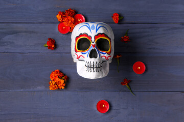 Wall Mural - Painted skull with marigold flowers and candles on blue wooden background. Celebration of Mexico's Day of the Dead (El Dia de Muertos)