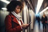 Fototapeta  - Young African American woman engrossed in smartphone scrolls through messages completely immersed in digital realm unaware of bustling commuters around in metro. Woman captivated by messages on screen