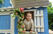 Cute little girl reaching out of the window in the playhouse while smiling at the camara