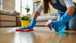 Housekeeper woman in blue rubber gloves using a spray and a duster while cleaning on floor at home