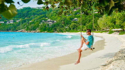 Wall Mural - Young men relaxing in a swing on the beach of Mahe Tropical Seychelles Islands. man on a luxury vacation at the Seychelles