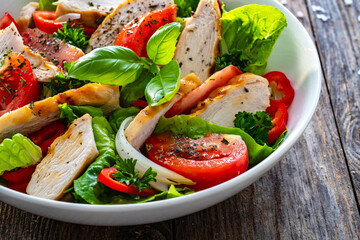 Wall Mural - Caesar style salad - grilled chicken breast and fresh vegetables on wooden table