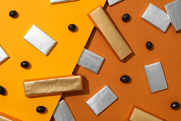 Wall Mural - Chocolates in foil and candies on orange background, top view