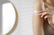 © New Africa - Woman applying body cream onto arm indoors, closeup. Space for text