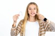 Beautiful teen blonde girl holding an invisible aligner and pointing perfect straight teeth. Dental healthcare and confidence concept.