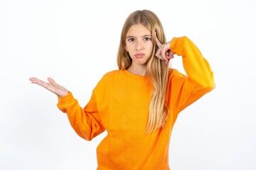 Beautiful caucasian teen girl wearing orange sweater confused and annoyed with open palm showing copy space and pointing finger to forehead. Think about it.