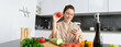 © Mix and Match Studio - Young woman orders groceries on mobile app. Girl in bathrobe sits in the kitchen with vegetables, looking for recipe to cook dinner, using smartphone application
