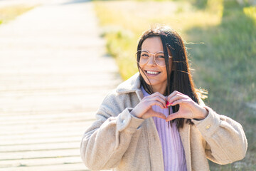 Wall Mural - Young woman at outdoors With glasses making heart with hands