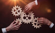 © Katsiaryna - Group of business people connecting wooden cogwheels together on black background
