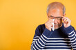 Portrait Asian senior old man sad wiping away his tears studio shot isolated on yellow background, Elder man crying raise glasses with tissue wipe red eyes, Sadness depressed lonely