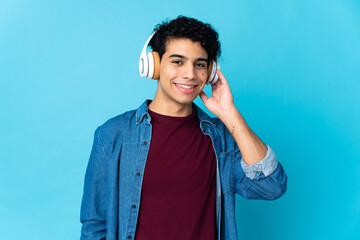 Young Venezuelan man isolated on blue background listening music