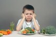 Fussy boy about vegetable dinner. Upset child at table showing disgust to broccoli and carrot. Generate ai