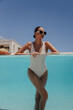 beautiful woman with dark hair in elegant swimming suit and accessories relaxing in swimming pool in summer beach club