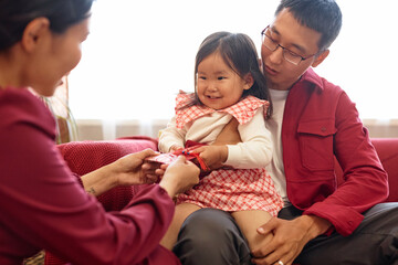 Wall Mural - Portrait of happy Chinese family exchanging gifts for New Year with mother giving red envelope to cute little girl